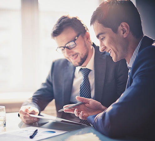 Image of two young businessmen using touchpad at meeting Image of two young businessmen using touchpad at meeting